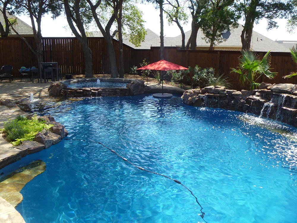 Sunlit freeform pool with rock waterfall and umbrella
